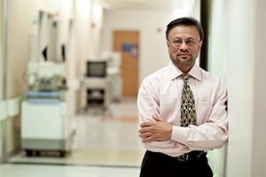 Physician standing against wall in hospital hallway.